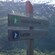 Two wooden arrow signs with Norwegian text and hiking symbols point towards a steep, verdant mountain
